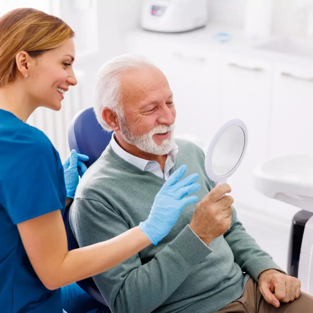 Eine Frau schaut auf das Gesicht eines Mannes, der im Zahnarztstuhl sitzt.