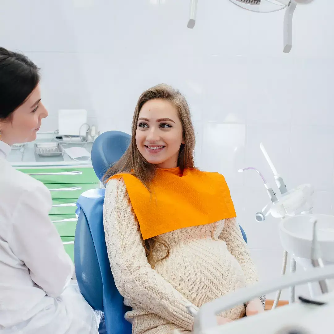 Eine schwangere Frau sitzt im Zahnarztstuhl und wird behandelt.